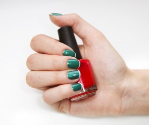 Manicure. Beauty treatment photo of nice manicured woman fingernails holding red nail polish. Feminine nail art with nice glitter, green and white nail polish
