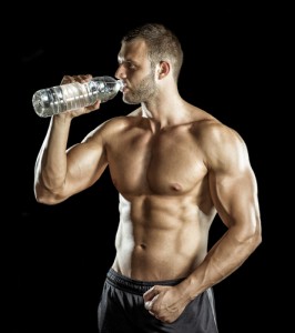Young adult man drinking water in gym.